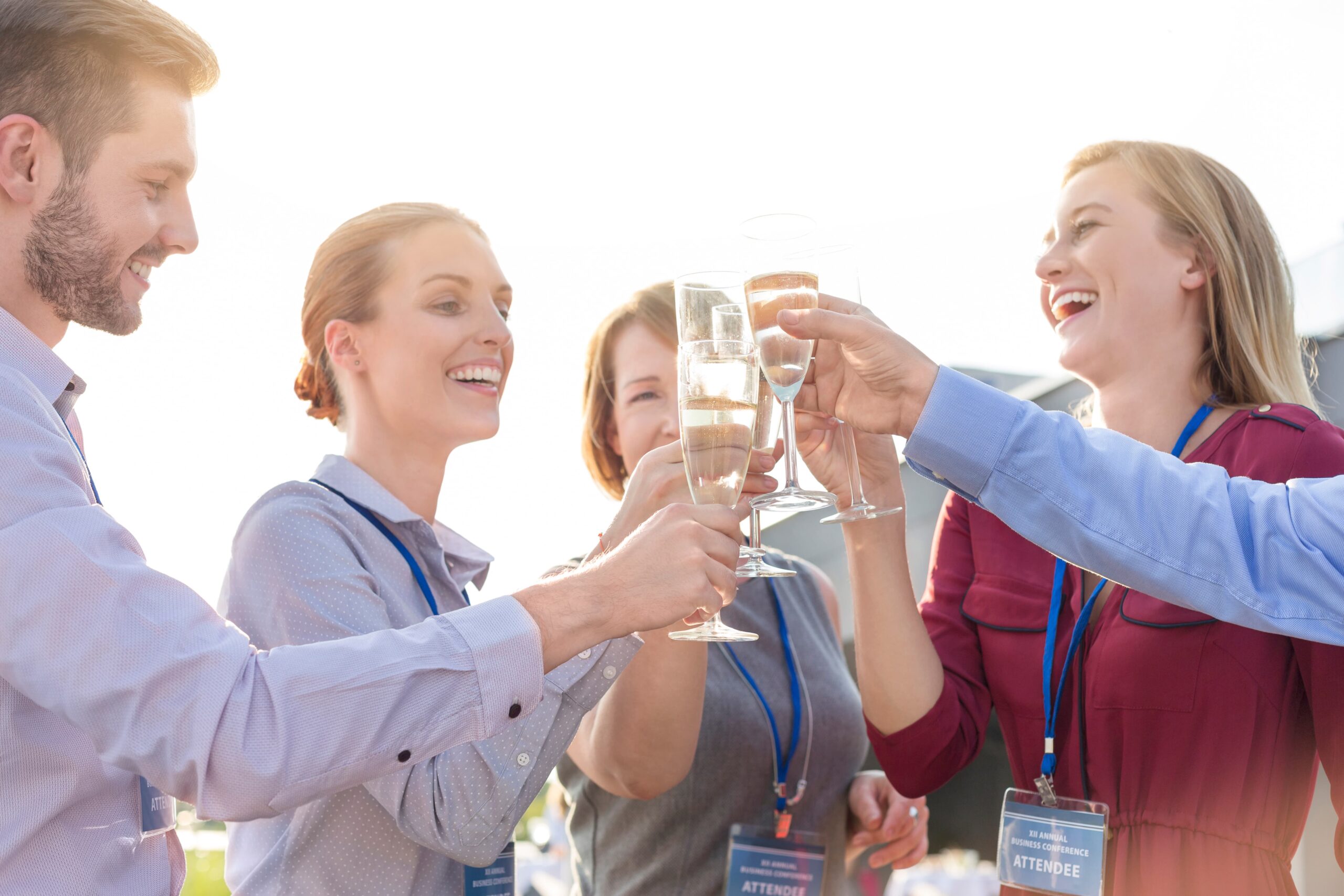 People laughing and toasting with champagne at a sunny outdoor party.